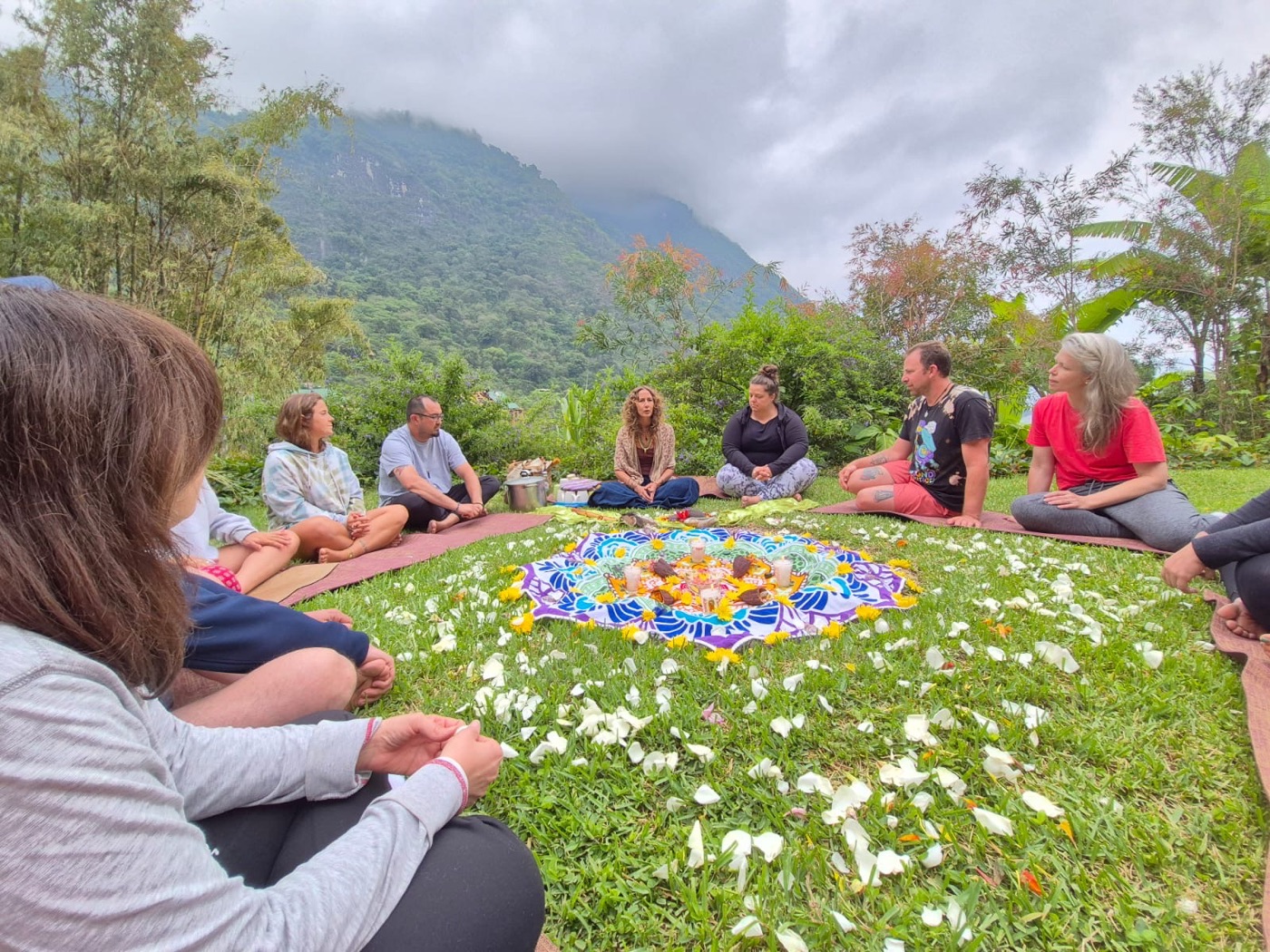 Retreat participants seated in a circle outdoors in a lush mountain setting