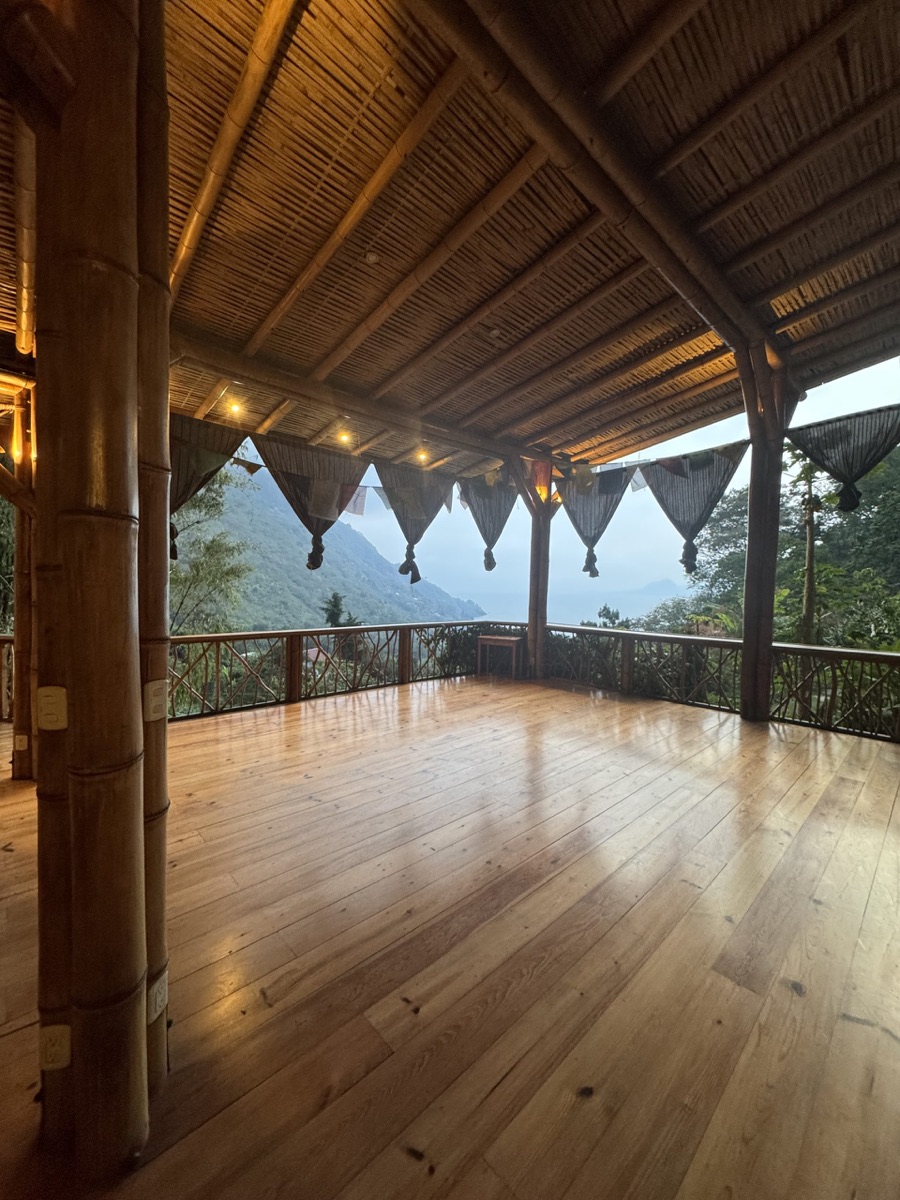 An open-air wooden retreat space overlooking green mountains and a lake